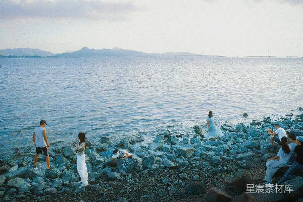 高清摄影 人们聚集在一座岩石海岸边， overlooking the ocean 可以翻译为“ overlooking the sea ”以符合中文表达习惯。