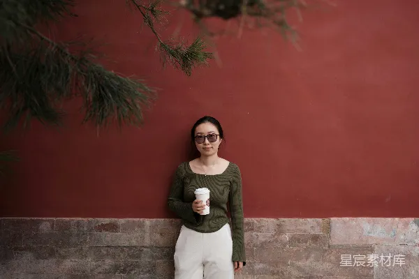 高清摄影 一位女性倚靠在墙上，手中拿着一杯咖啡。