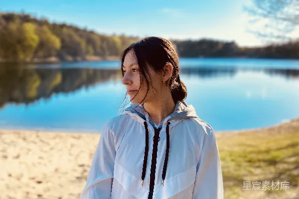 高清摄影 白上衣连帽风衣的女人站在近水的白色沙滩上，白天。