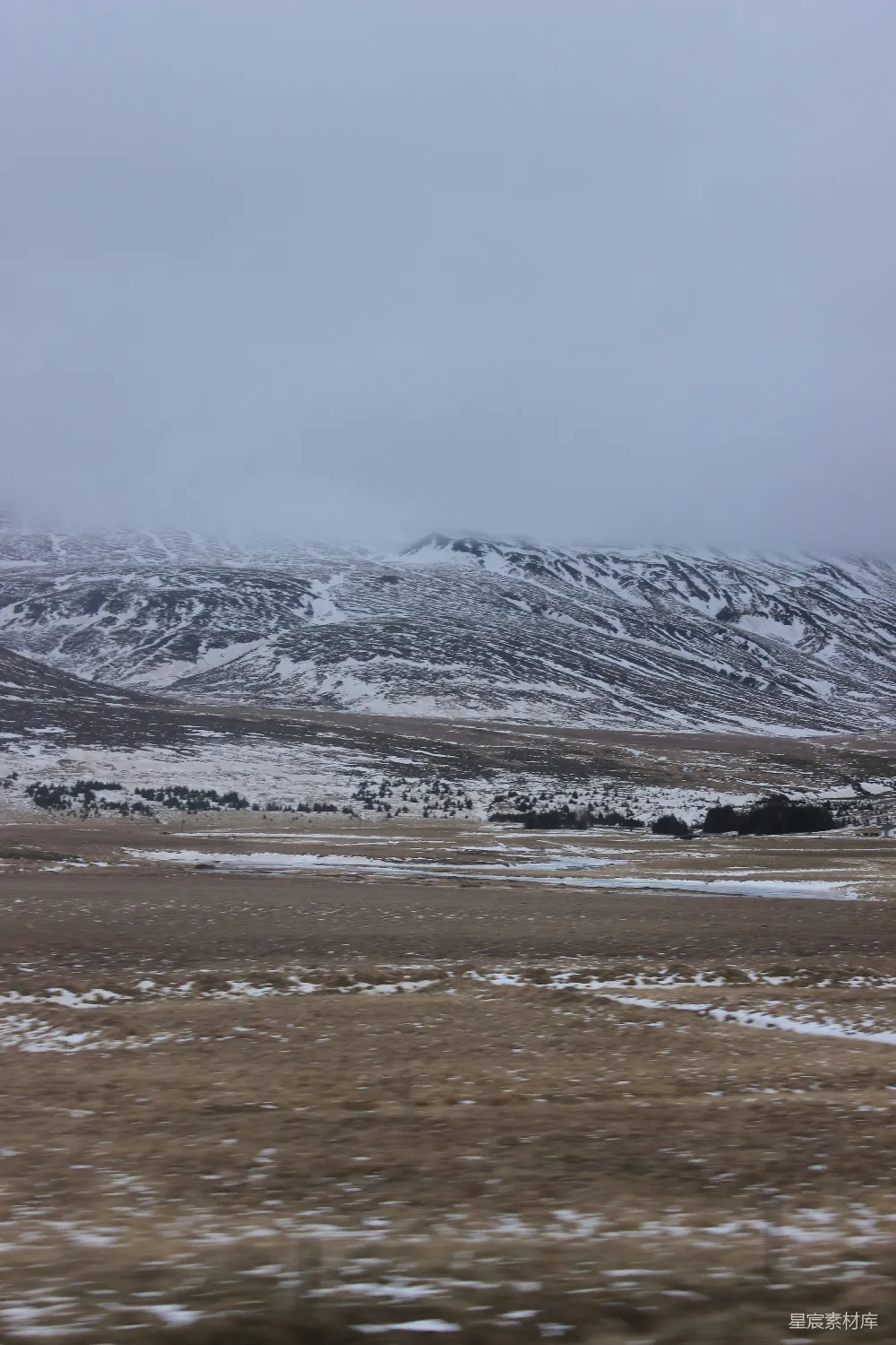 高清摄影 远处一片白雪皑皑的山峦，在 foreground 有一片田野。