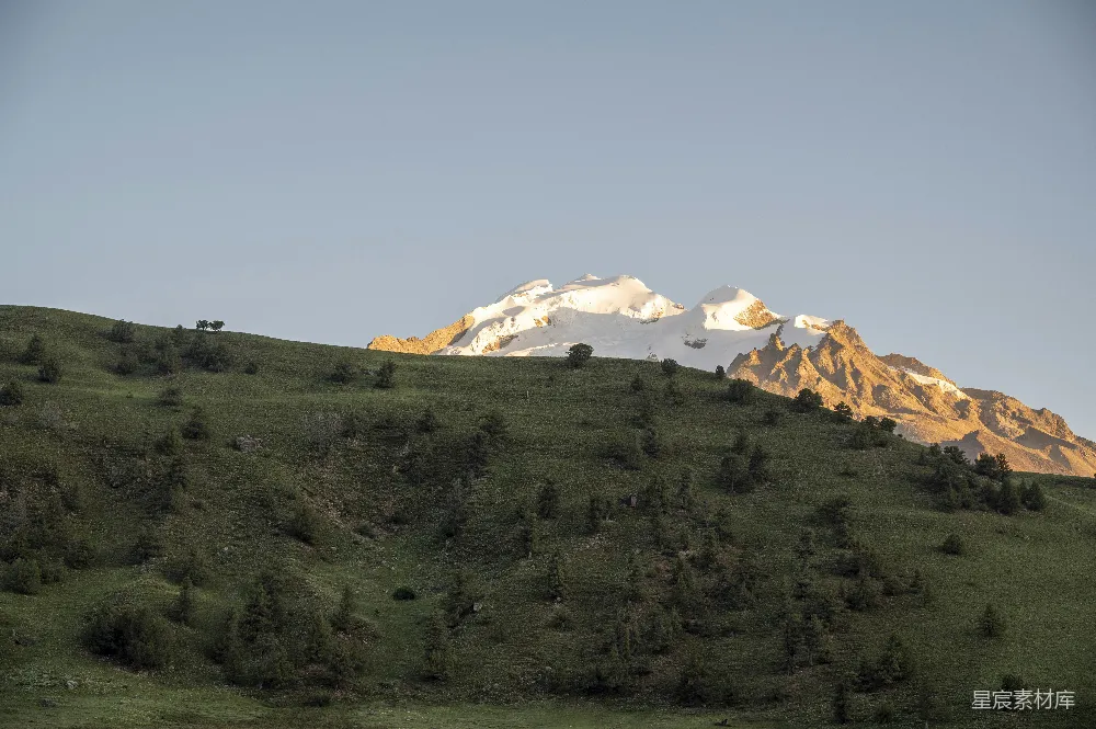 高清摄影 自然 旅行 雪山之巅在金色阳光的照耀下闪耀，背景是绿色的丘陵。