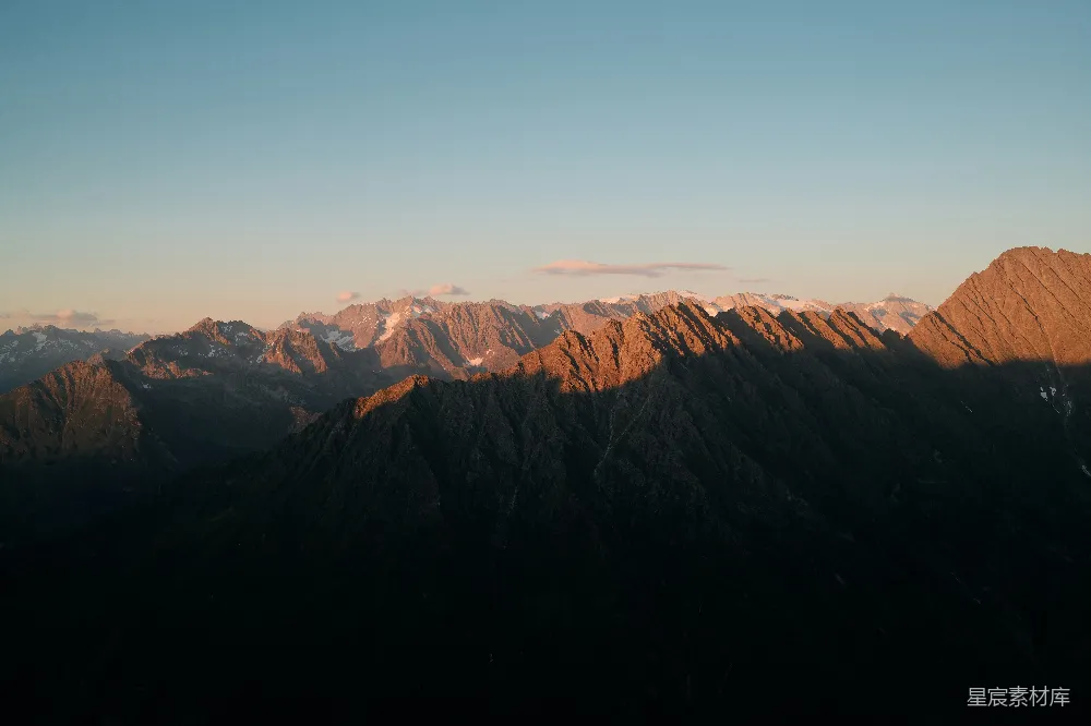 高清摄影 夕阳映照着山峰顶部的崎岖山峰，金光闪耀。