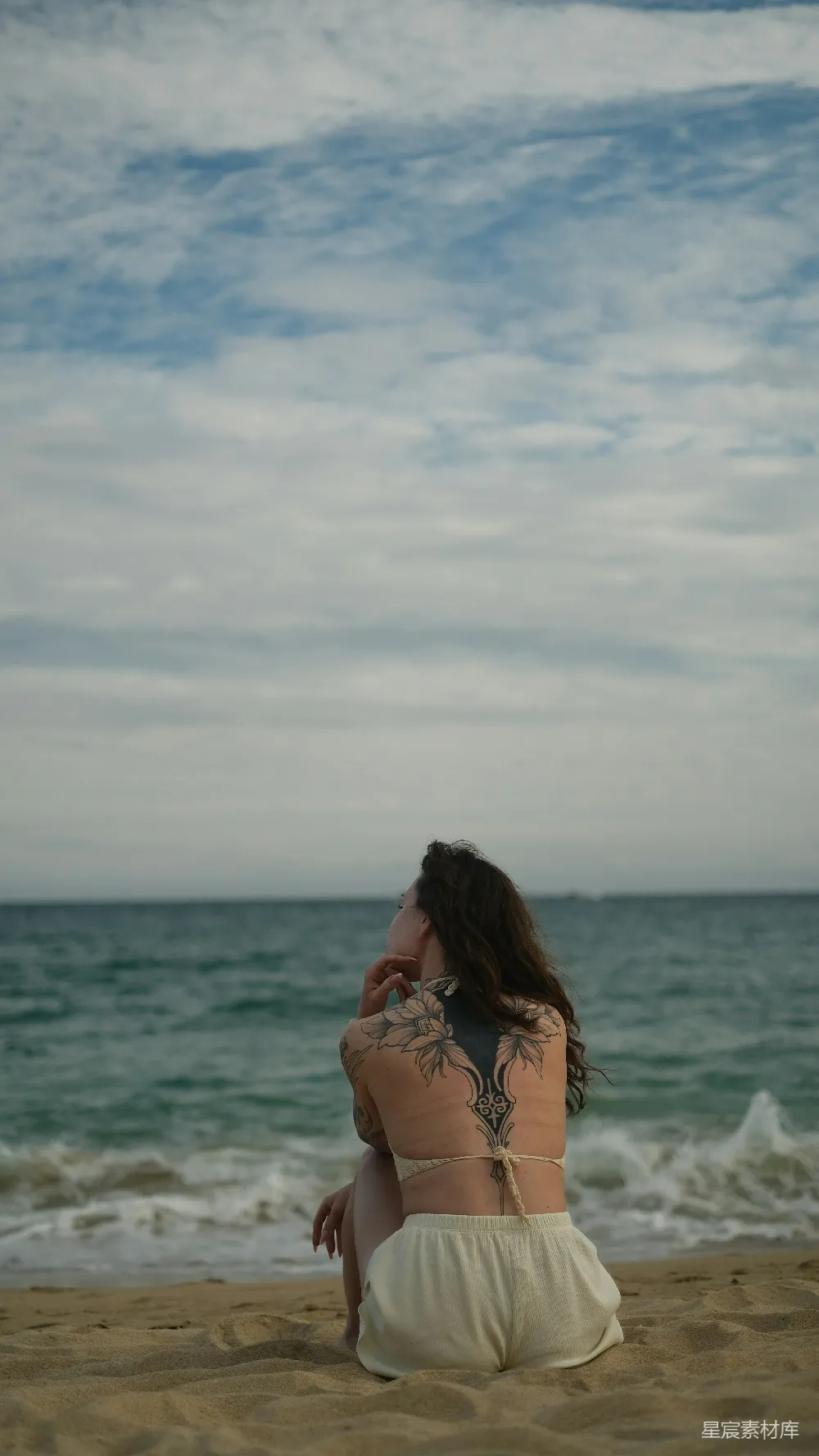 高清摄影 有纹身的妇女坐在海边。