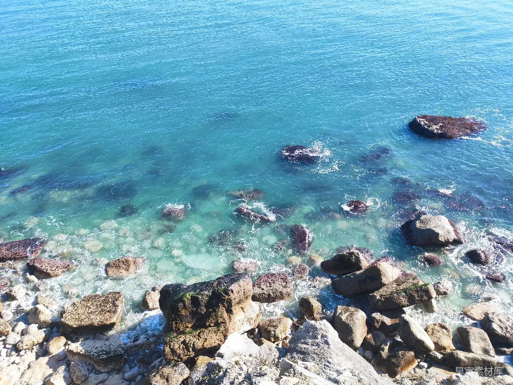高清摄影 一块岩石嶙峋的海滩，清澈的蓝色海水和大大小小的石头。