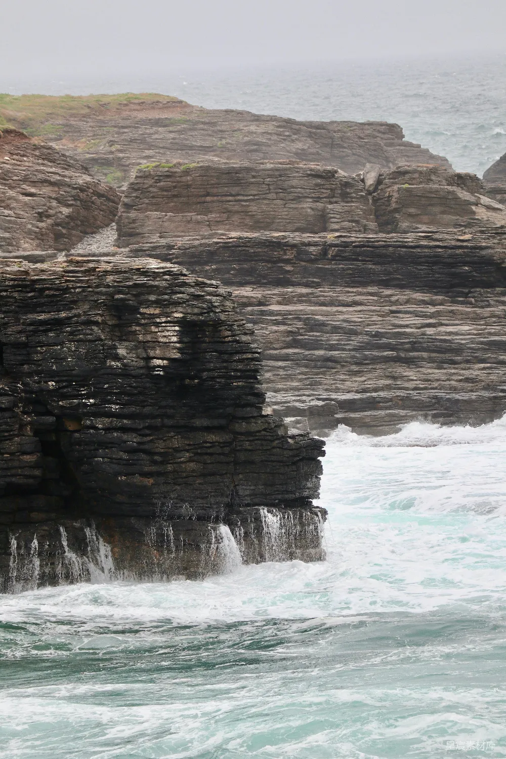 高清摄影 海浪拍打着黑暗而层叠的海岸峭壁。