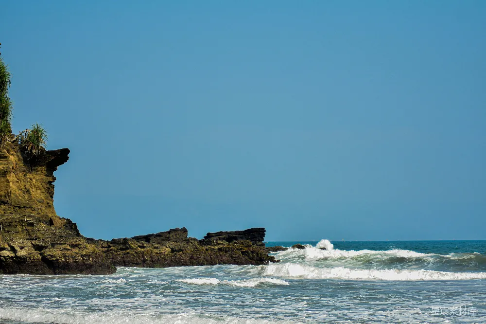 高清摄影 海滩上一块岩石露出物，海浪在其前方拍打。