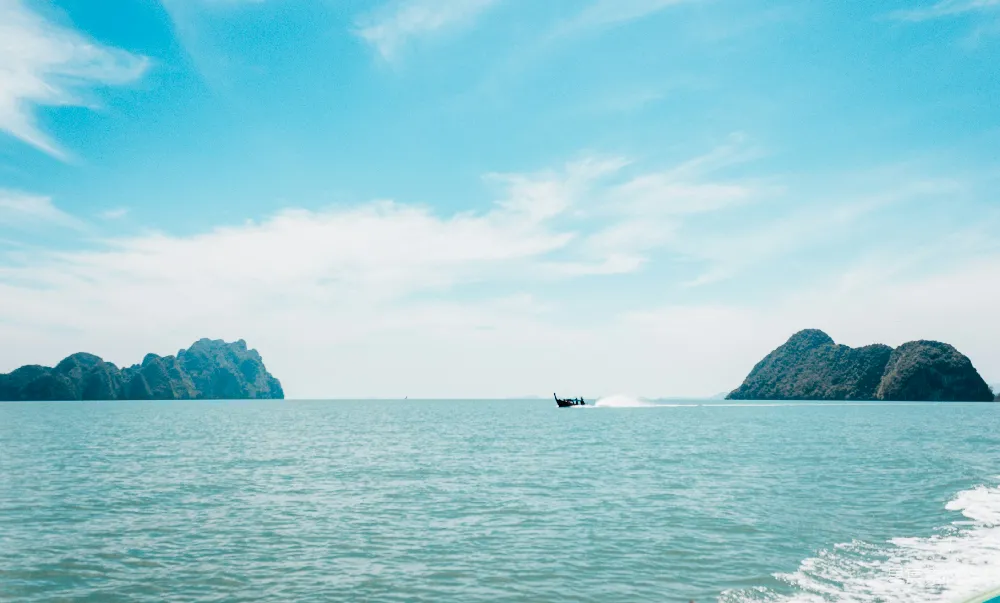 高清摄影 白天小船在海中靠近岛屿航行，天空湛蓝。