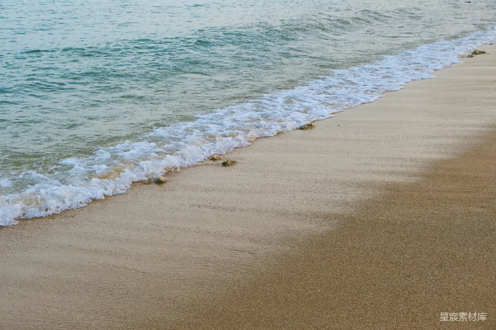 高清摄影 一片沙子铺就的海滩，海浪涌向岸边。