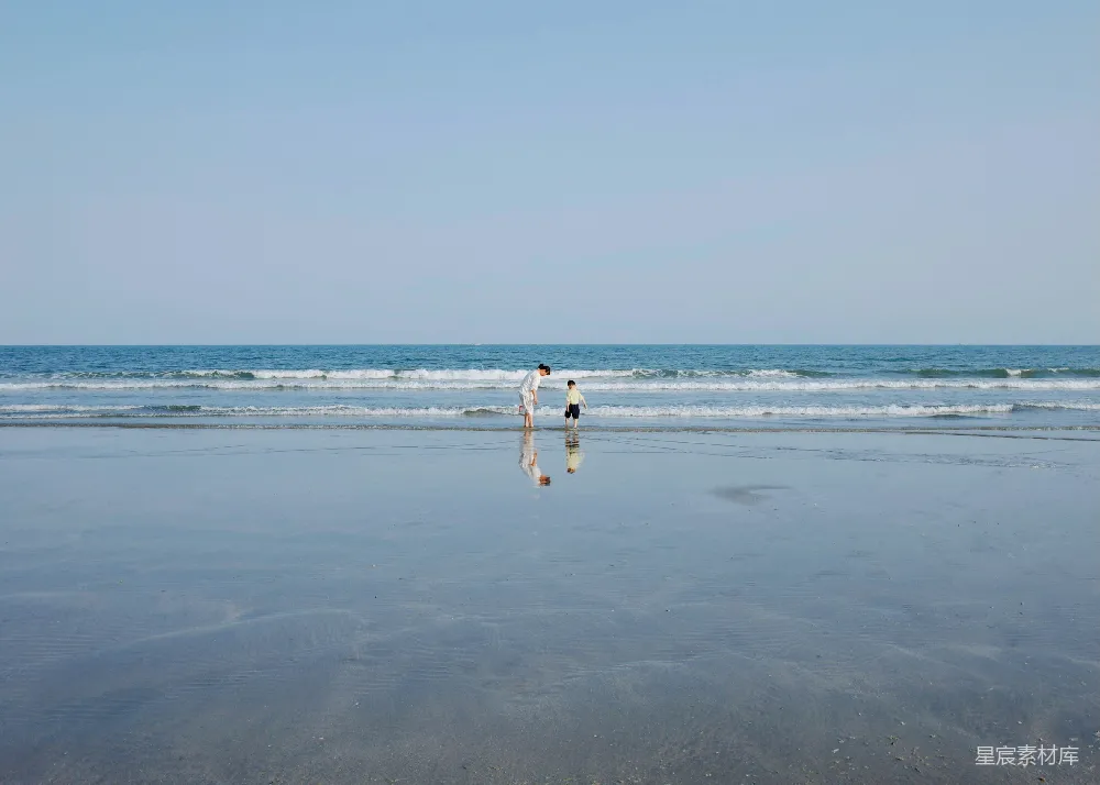 高清摄影  人们站在海滩上，旁边是倒影。