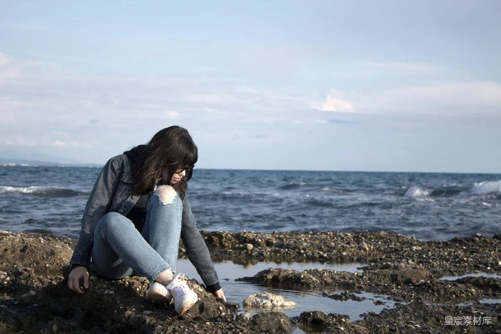 高清摄影 一个女人坐在岩石海滩旁的海边。