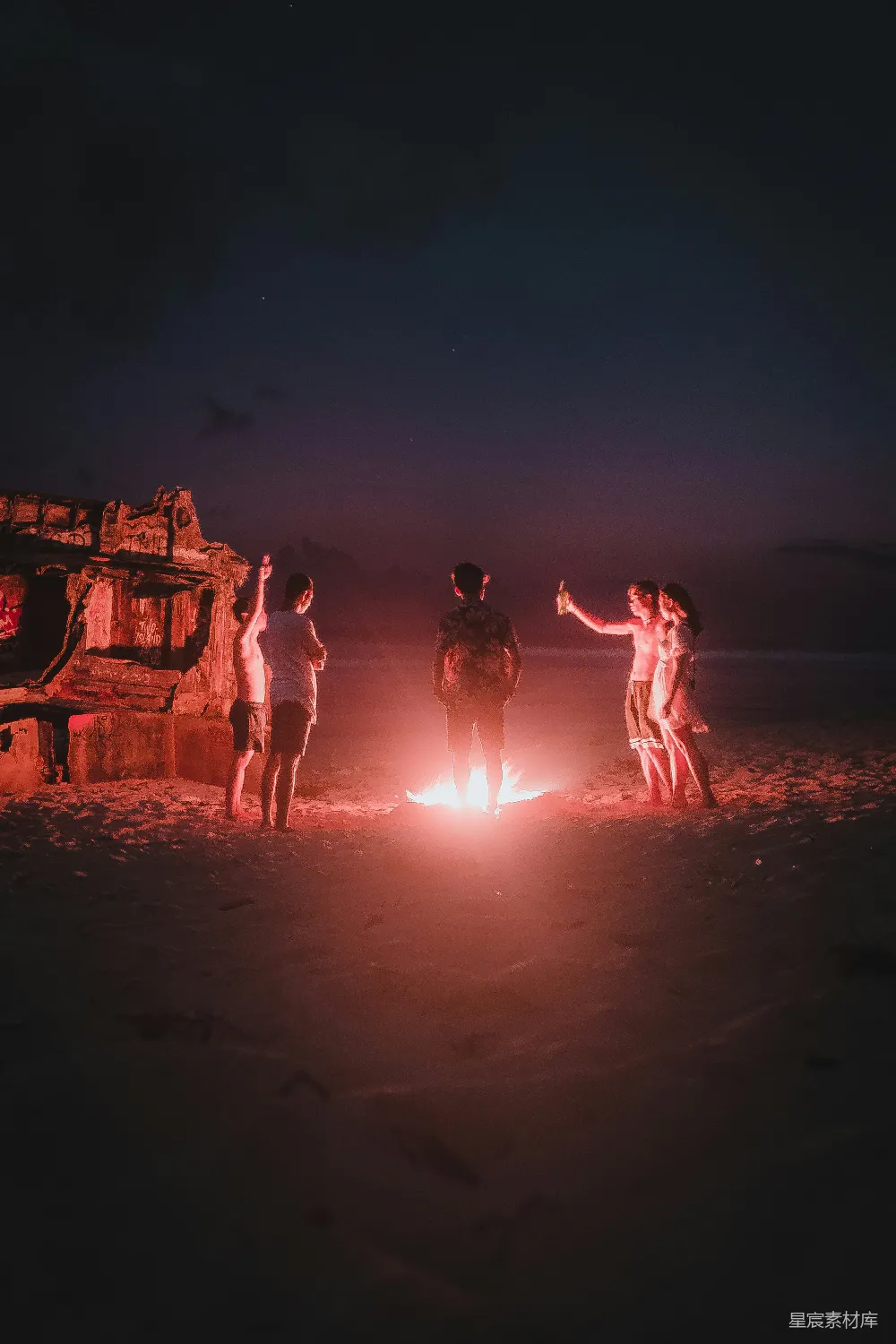 高清摄影 一群人在海滩岸边在夜间站立。