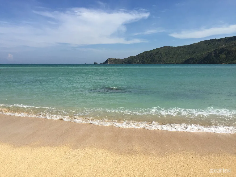 高清摄影 海边有波浪，背景有一座小山。