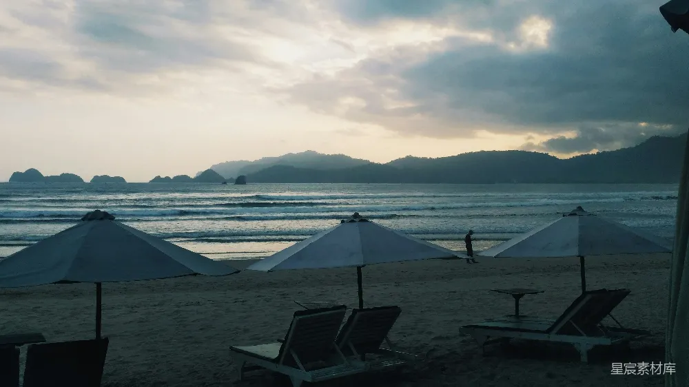 高清摄影  海滩上的躺椅和遮阳伞，背景是山峦。