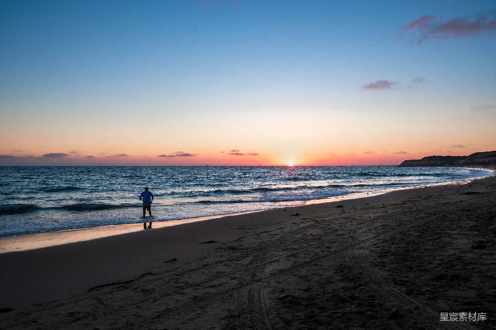 高清摄影 黑衣男子在海滩上夕阳西下时漫步。