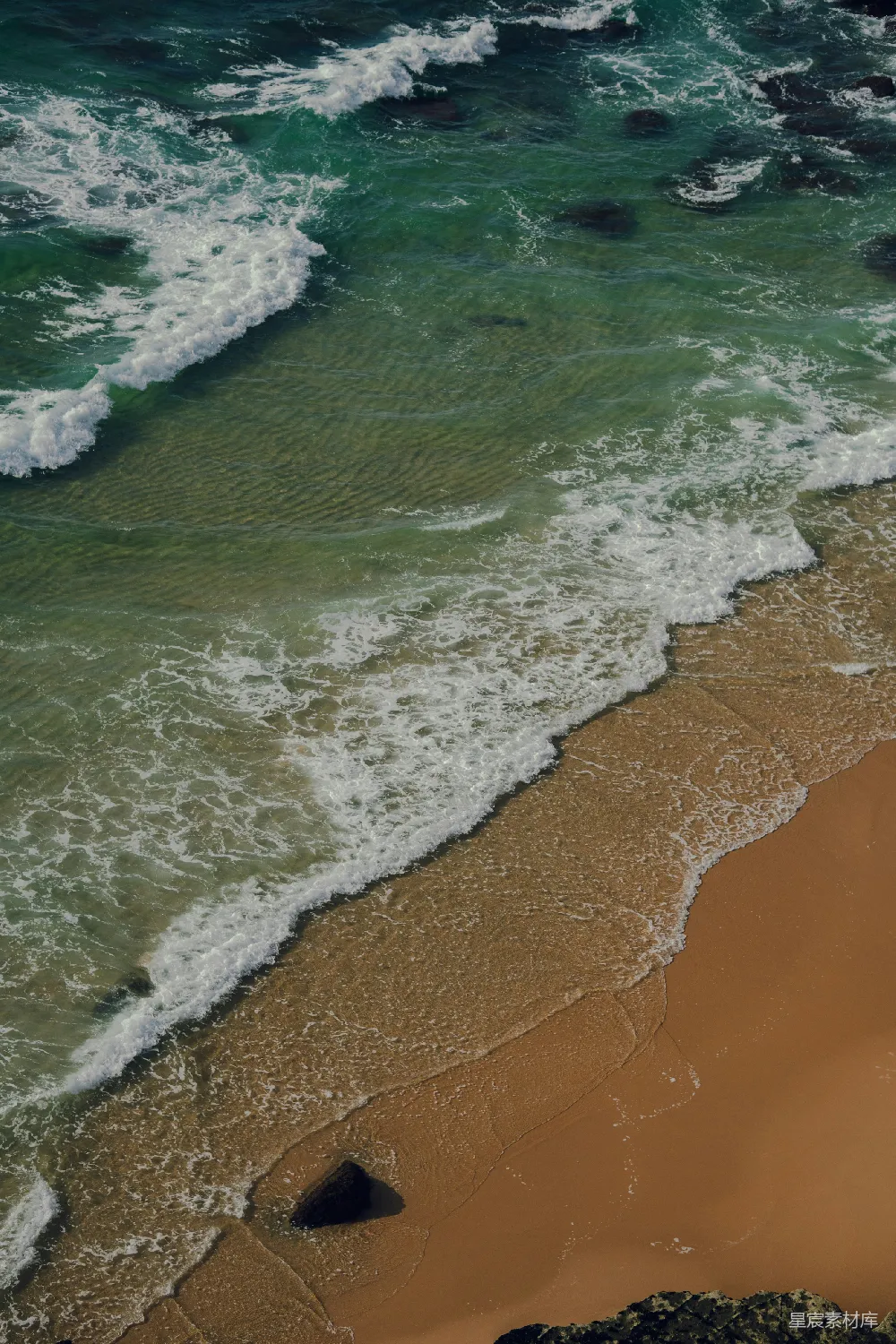 高清摄影  海边的一片沙滩，旁边是波涛汹涌的海洋。