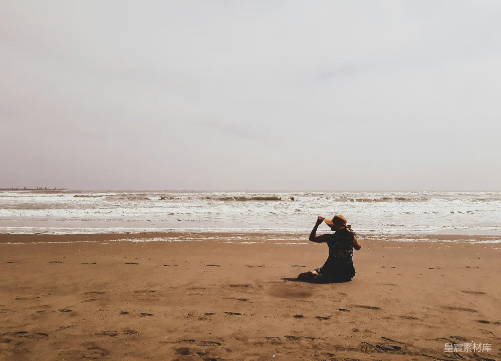 高清摄影 一位妇女坐在海滩上望着大海。