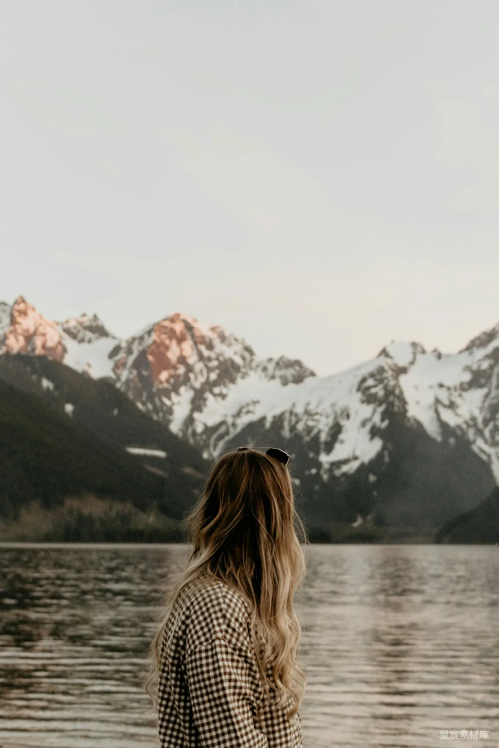 高清摄影 一个女人站在湖边，背景是山脉。