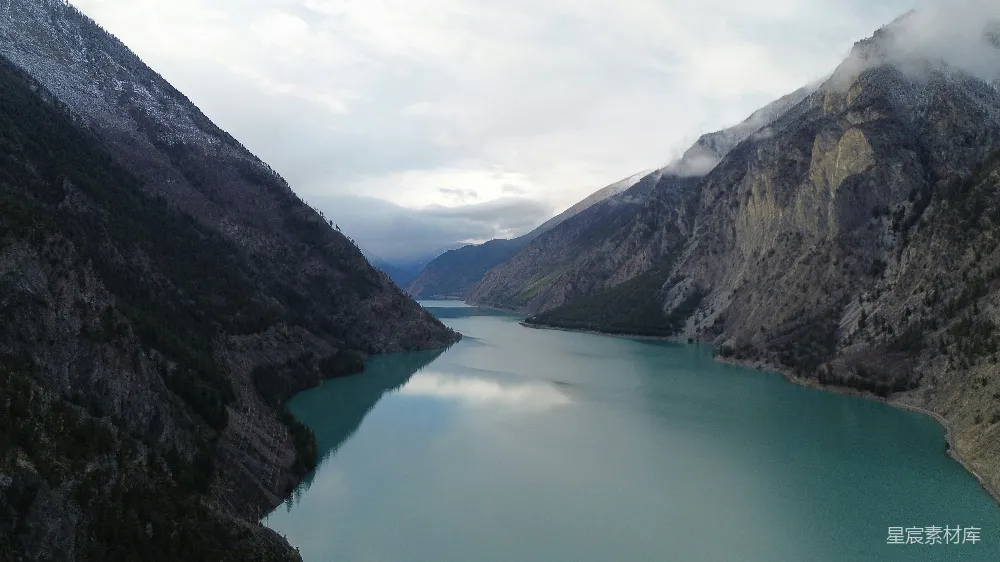 高清摄影 云层下，位于陡峭岩石山脉之间的蓝绿湖泊