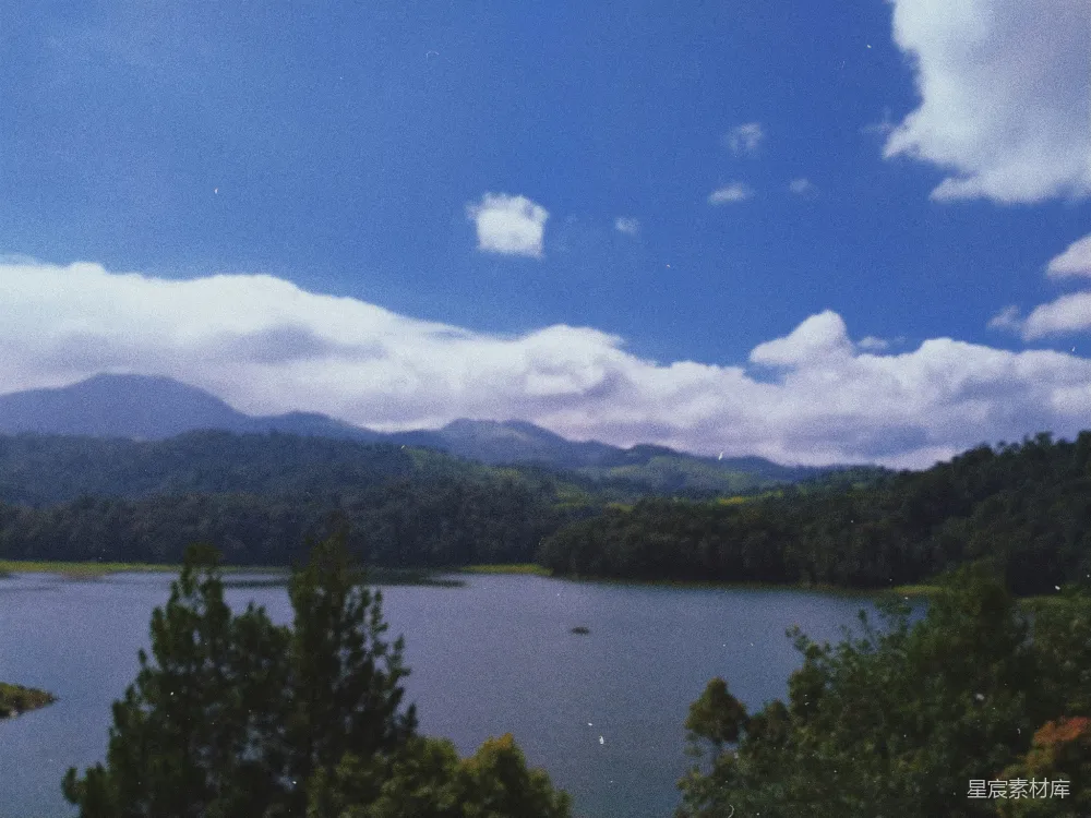 高清摄影 一片被树木和山峦环绕的湖泊，在蓝天之下。