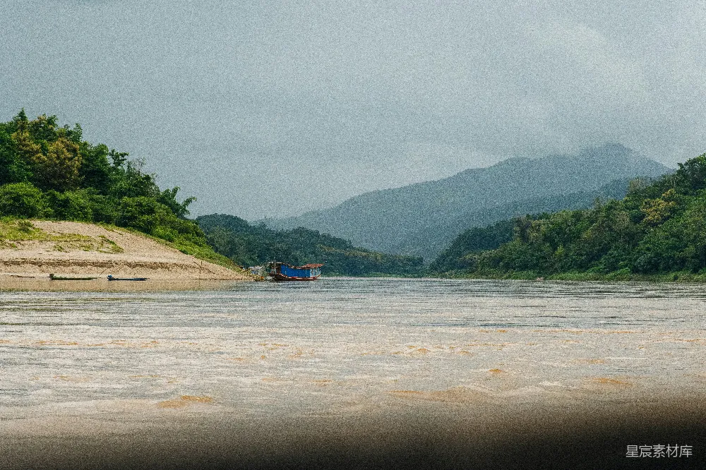 高清摄影 一艘船漂浮在河边，旁边是茂密的绿色森林。