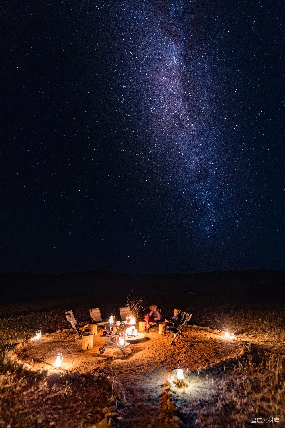 高清摄影 一群人在满天星辰闪烁的夜空中围坐在篝火旁。