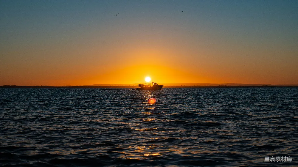 高清摄影 夕阳西下，海天相接处有一艘船隐约可见。