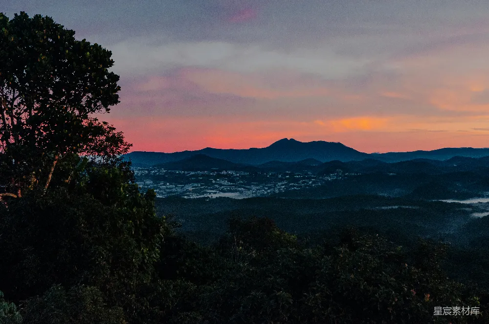 高清摄影 山脚下一片山峦的夕阳美景，前景中有一棵树。