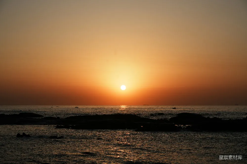 高清摄影 夕阳西下，海平面上有岩石在 foreground。
