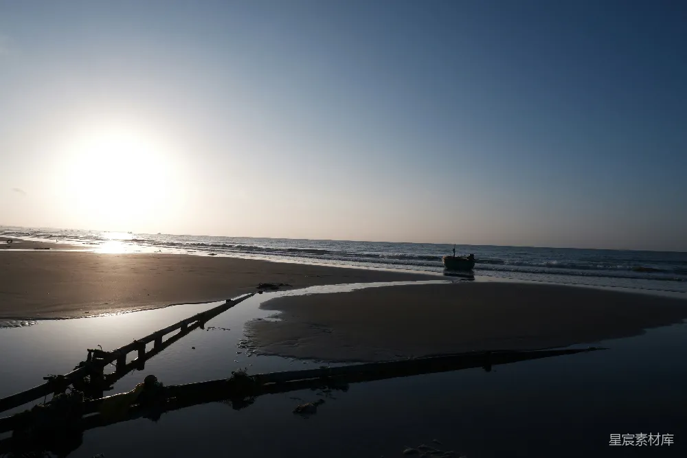 高清摄影 夕阳照亮一片沙滩、大海和一根黑色的管子。