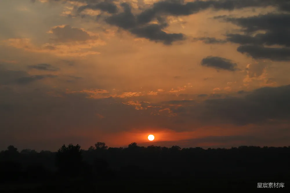 高清摄影 夕阳西下，一片田野旁有树木。