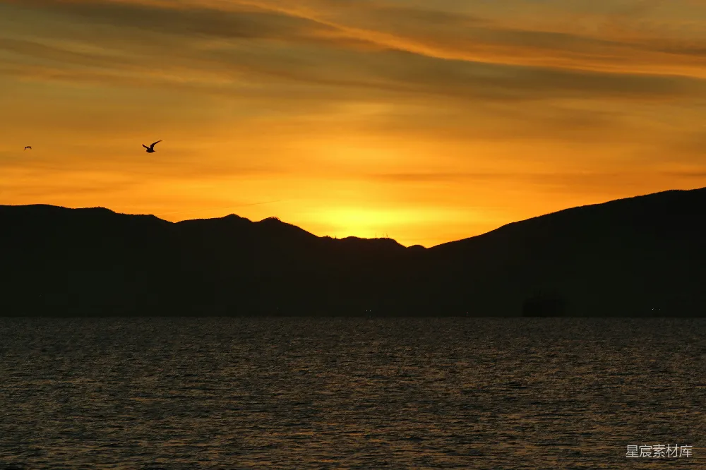 高清摄影  夕阳映照在一片水体上，山峦在背景中若隐若现。
