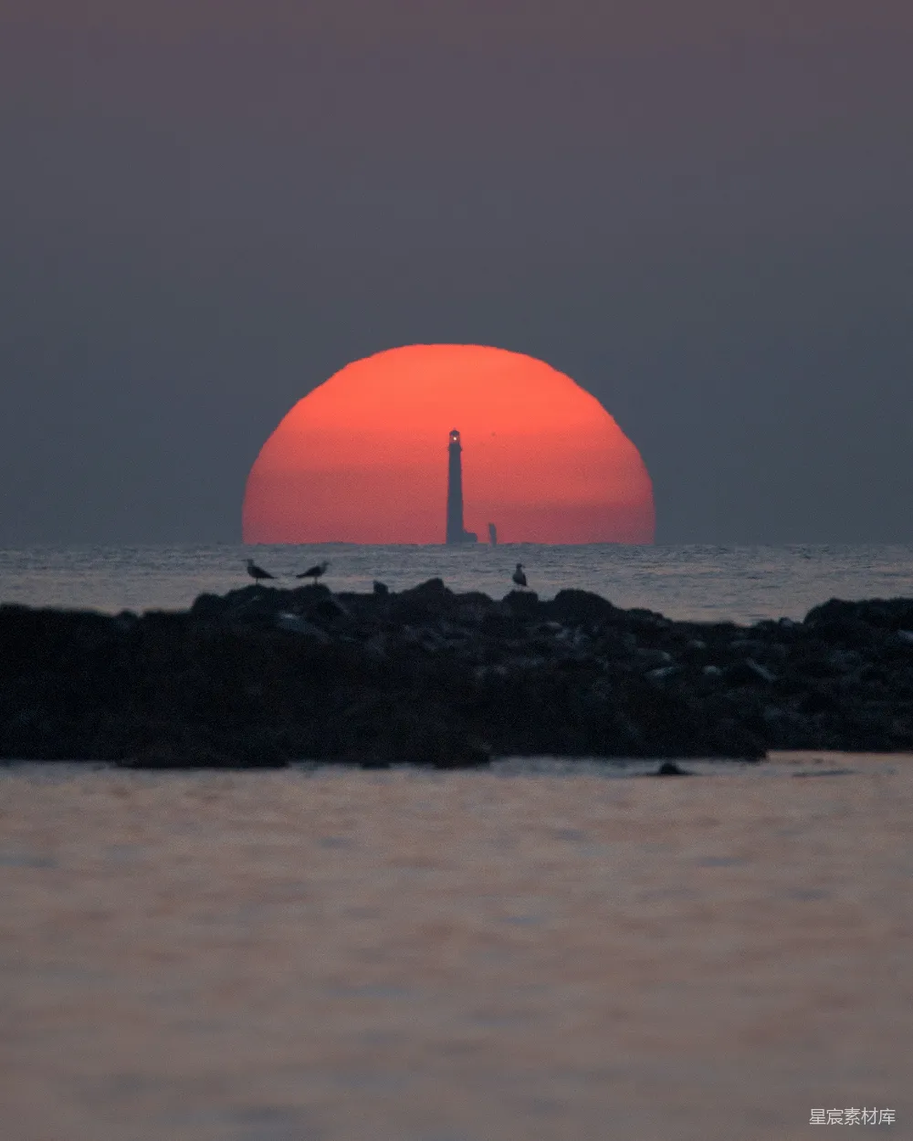 高清摄影 夕阳下橙色球体靠近黑色岩石附近，周围环绕着水面。