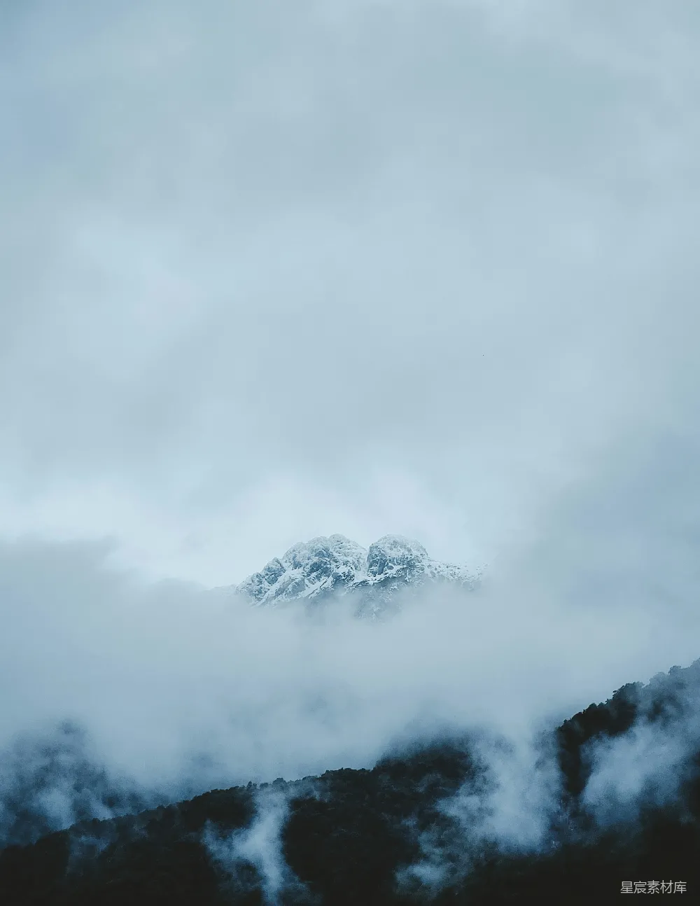 高清摄影 远处有一座被云层覆盖的山峰，山顶积雪皑皑。