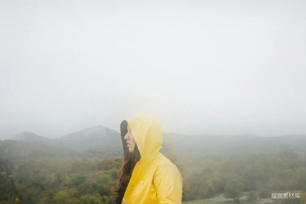 高清摄影 一个穿黄雨衣的女人站在山顶上。