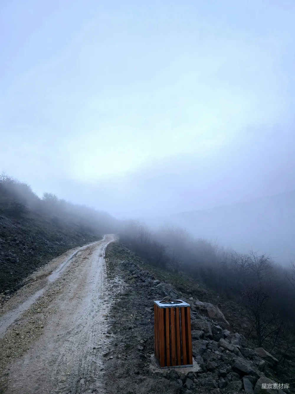 高清摄影 一条尘土路蜿蜒穿过一片雾气缭绕的山地景观。