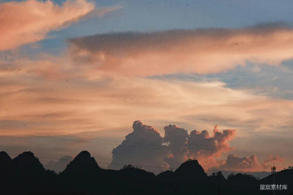 高清摄影 夕阳下， dramatic 粉色云朵映衬着轮廓分明的山峰。
