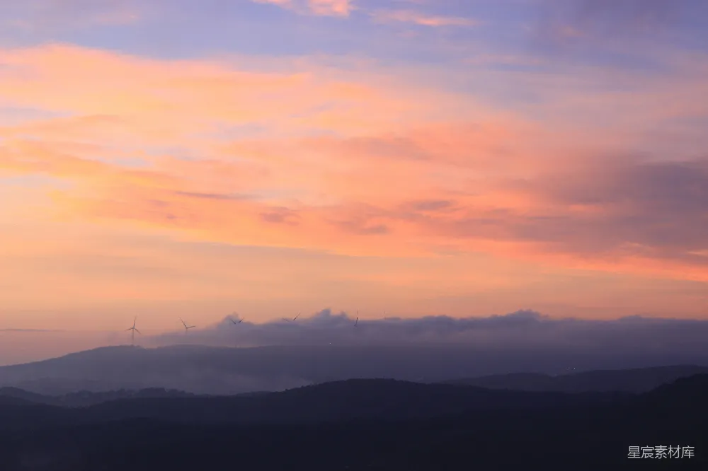 高清摄影 夕阳下，淡粉色的云层覆盖在深色山峦之间。