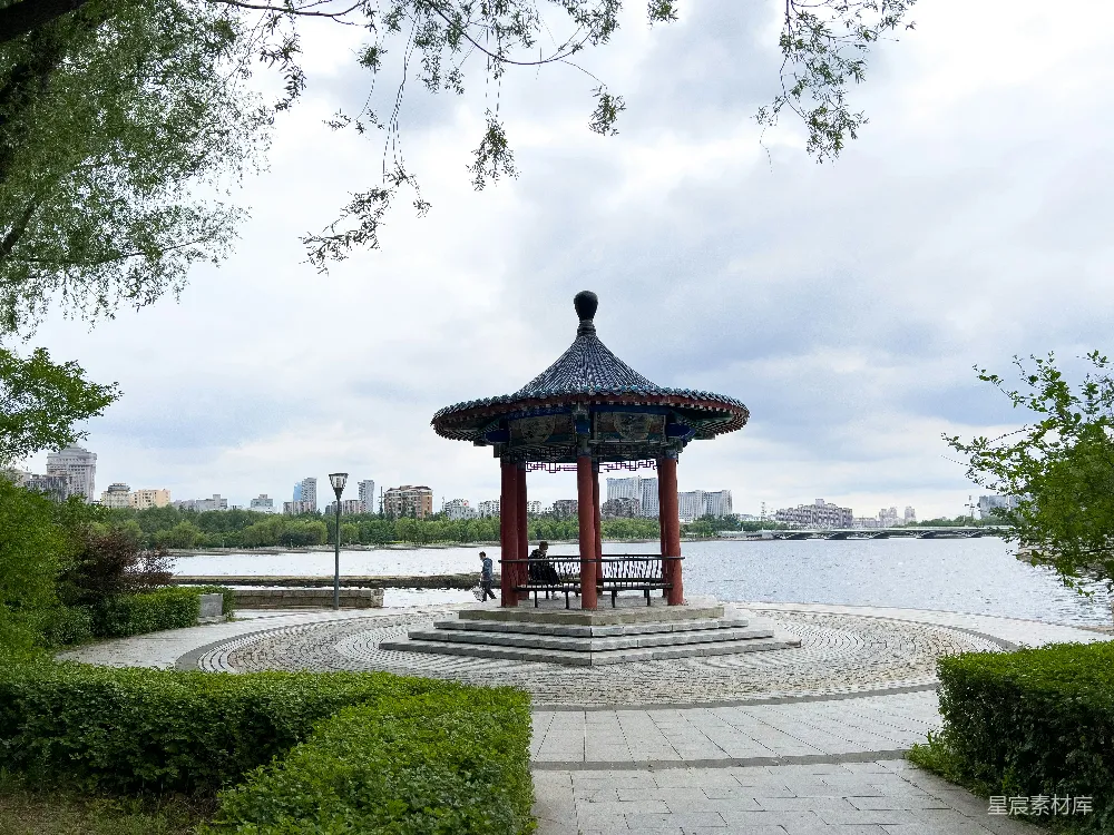 高清摄影 一个凉棚坐落在公园中，旁边有一片水域。