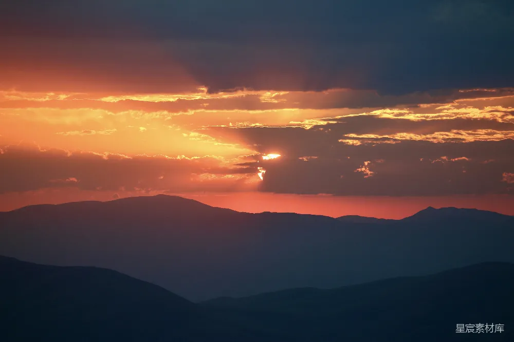 高清摄影 夕阳映照着轮廓分明的山峦群落，云彩显得格外 dramatic（戏剧性的）。
