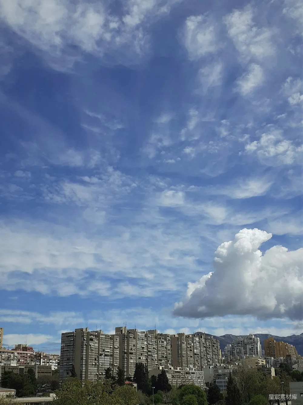 高清摄影 一座城市在天空中矗立着高大建筑物的景象，背景是阴云笼罩下的蔚蓝天空。