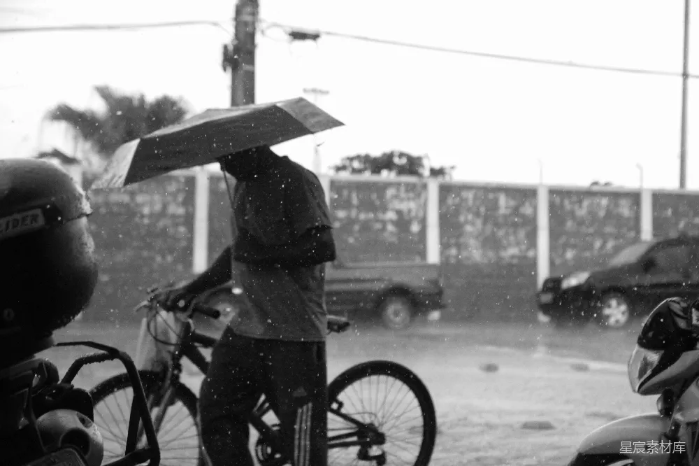 高清摄影 伞下行人骑自行车在雨中漫步。