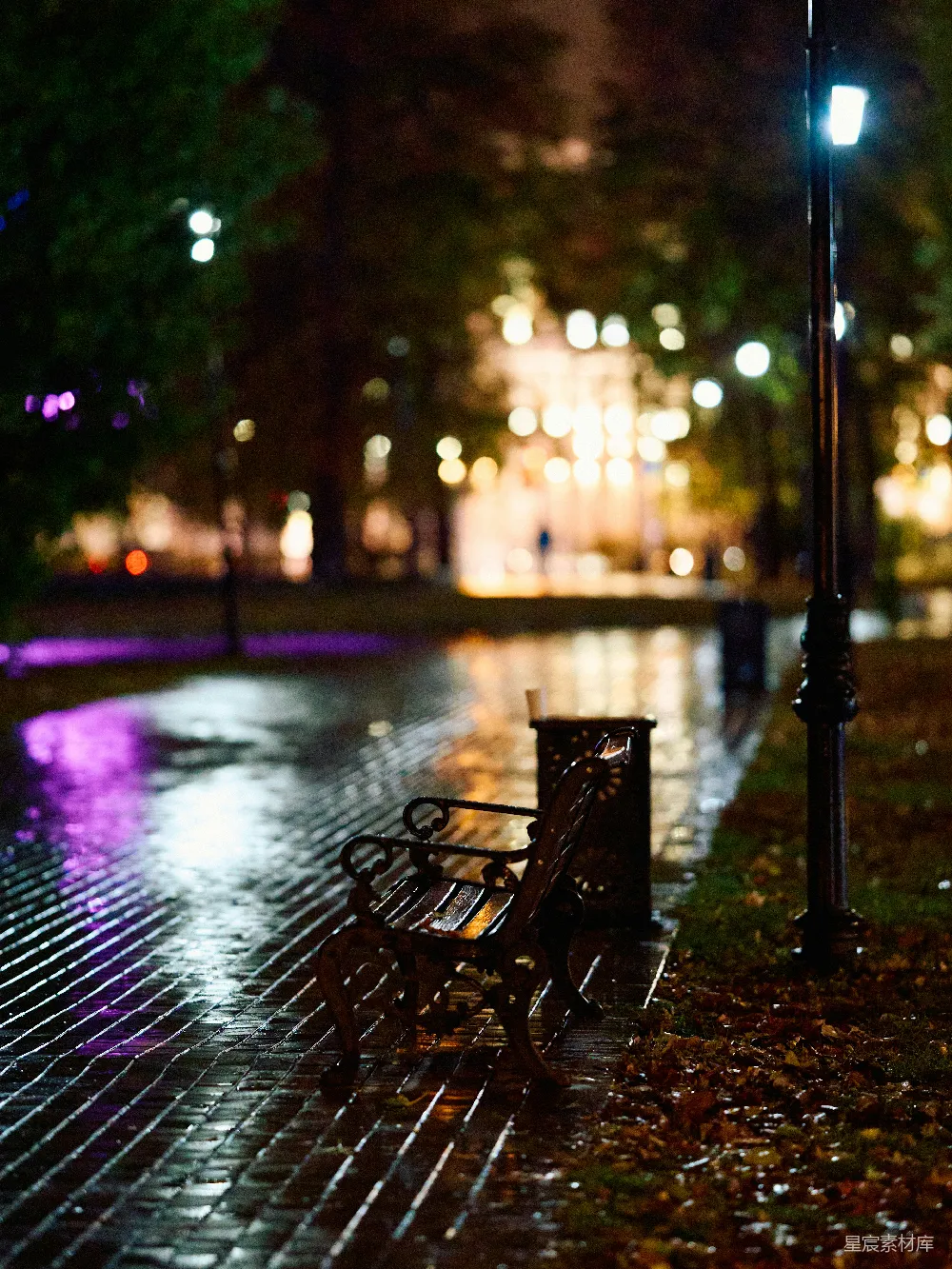 高清摄影 夜晚公园长椅上坐着一个人，旁边是湿漉漉的 sidewalk 。