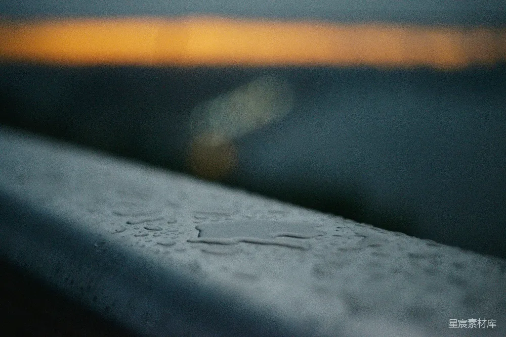 高清摄影 铁栏杆上的水滴，背景是模糊的落日。