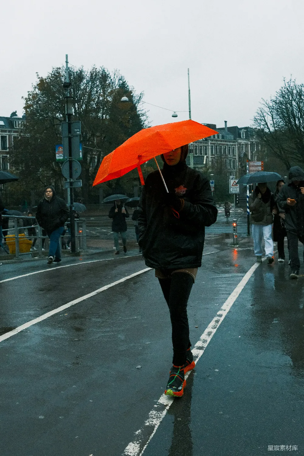 高清摄影 手持橙色伞的人在雨中行走。