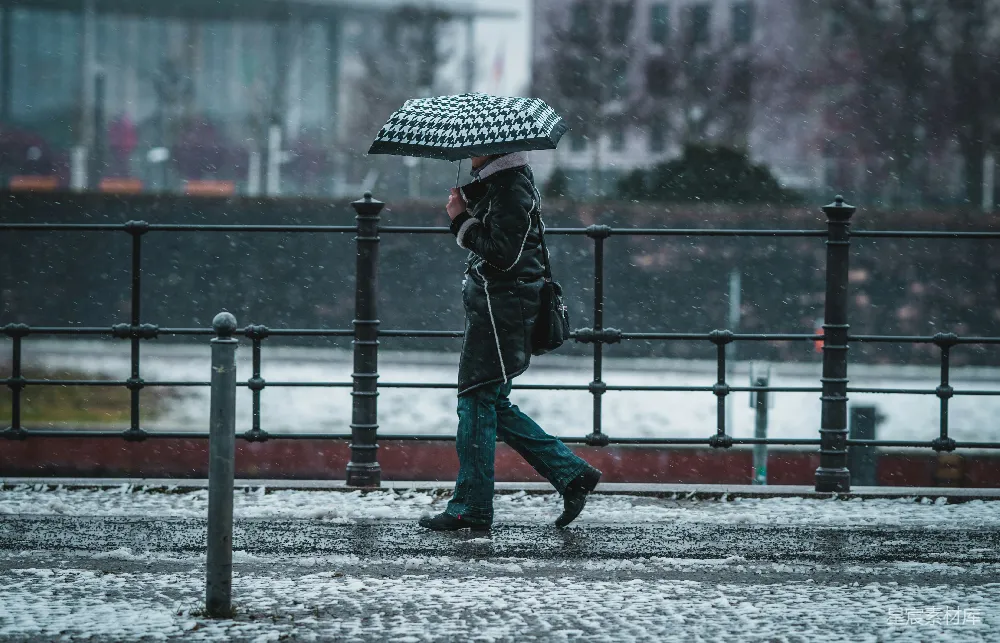 高清摄影 黑色夹克和蓝色牛仔裤的人手持雨伞在覆盖着白雪的道路中行走。