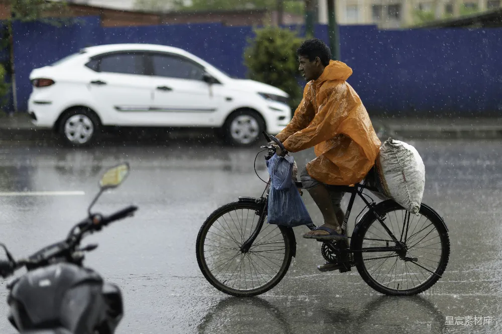 高清摄影 橙色雨衣的人骑自行车带着一个袋子在下雨。