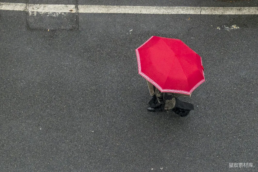 高清摄影 红色雨伞下的行人正在灰色的柏油路上白天行走。