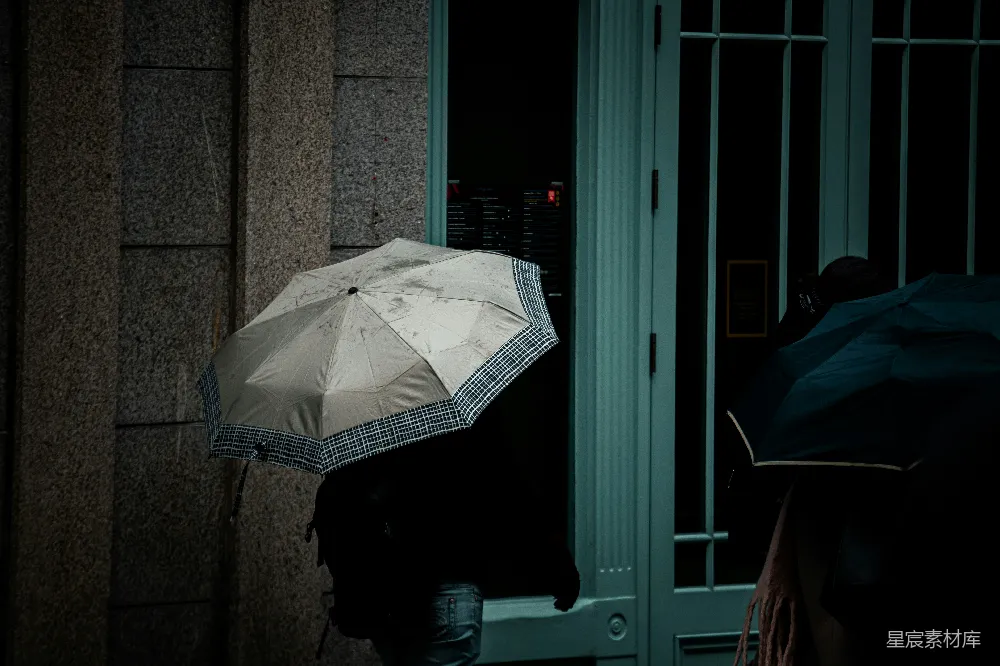 高清摄影 夜晚行人手持雨伞走过一栋建筑旁。