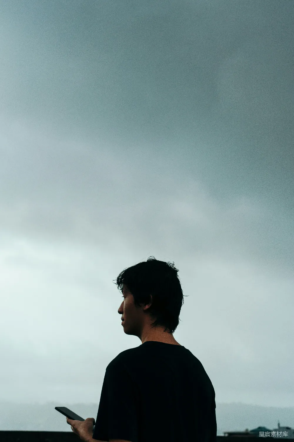 高清摄影 一个男子站在一片乌云密布的天空下，手持着手机。