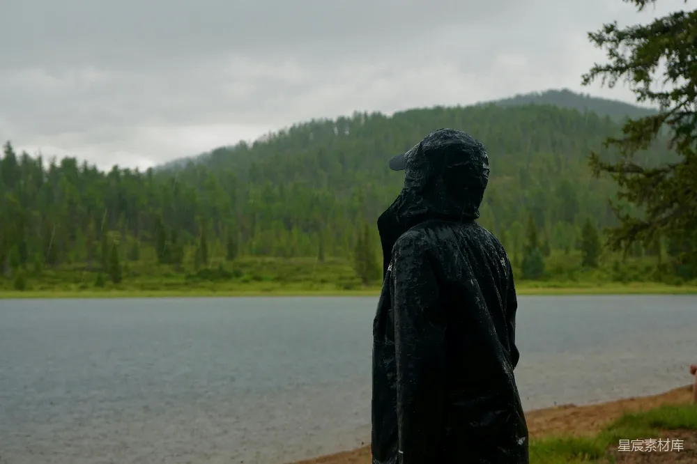 高清摄影 穿着雨衣的人望着湖上的雨。